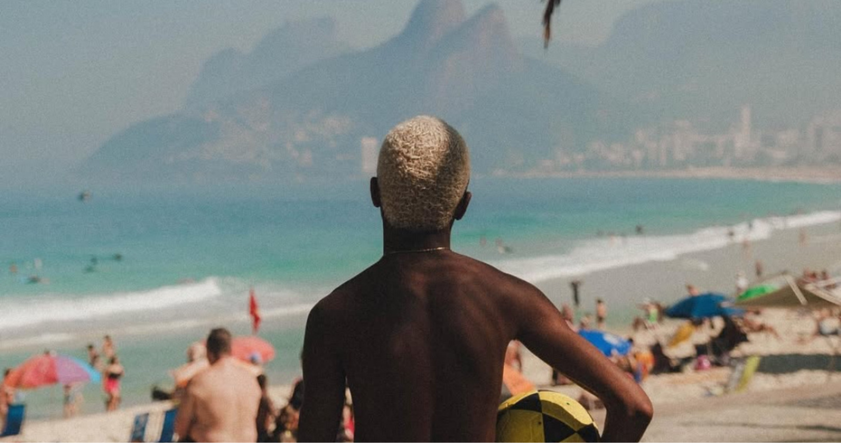 Kid on beach in rio with ball under arm staring at sugarloaf monolith with dreams of making it as a pro footballer